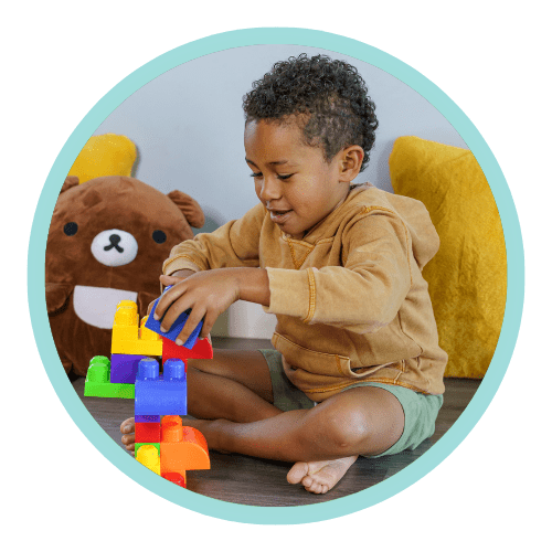 An adorable preschool age black boy builds a structure with large and colorful plastic toy blocks. The creative and curious child is having fun at school or daycare. Learning, school, child care and family concepts.